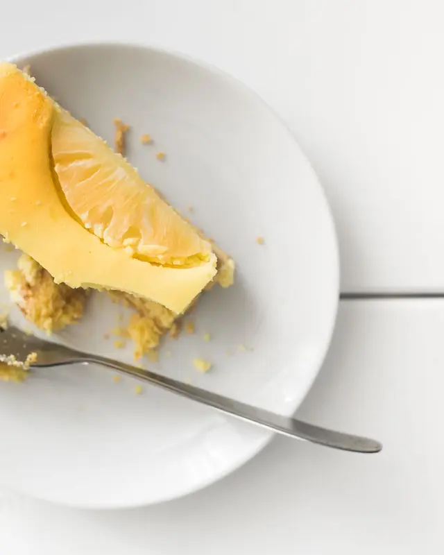 Fetta di cheesecake al limone su piatto bianco, con una forchetta appoggiata di lato