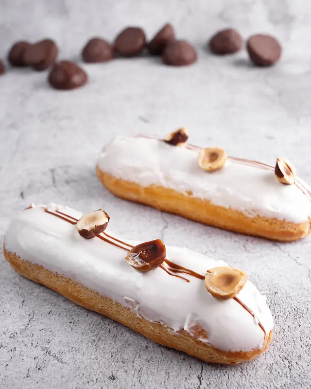 Due éclair glassati di bianco e decorati con nocciole, su un piano di pietra chiara