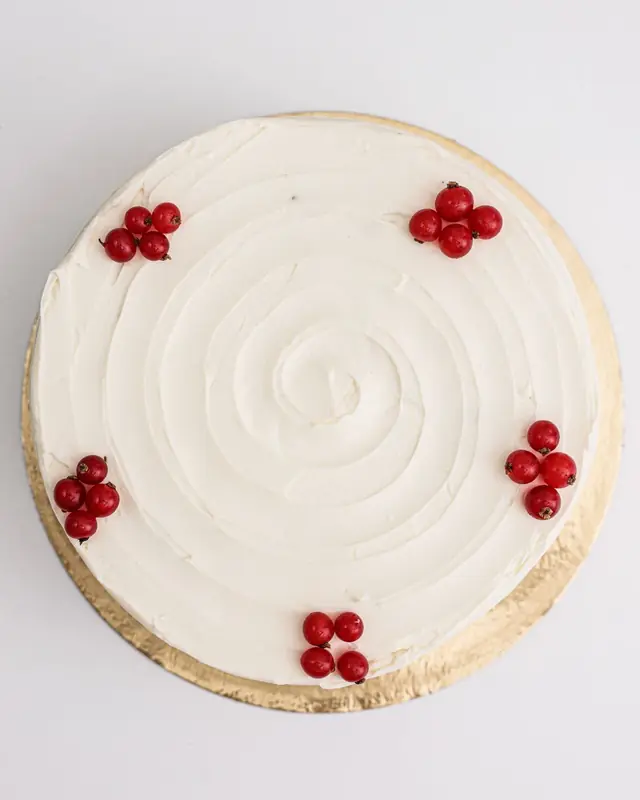 Torta rotonda ricoperta di panna montata e decorata con ribes rossi, vista dall'alto