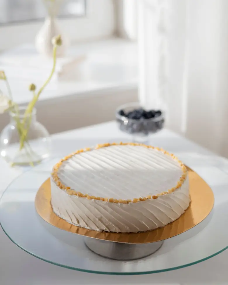 Torta bianca rifinita a spatola su un'alzata di vetro, accanto a una finestra
