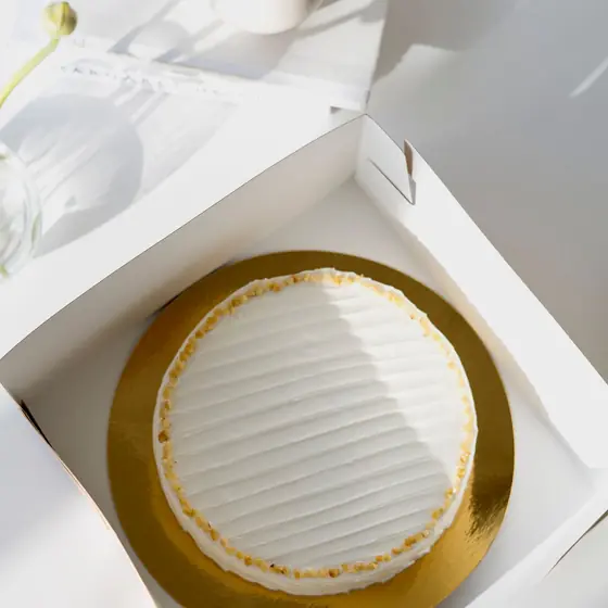 Torta bianca su vassoio dorato dentro la scatola aperta della pasticceria